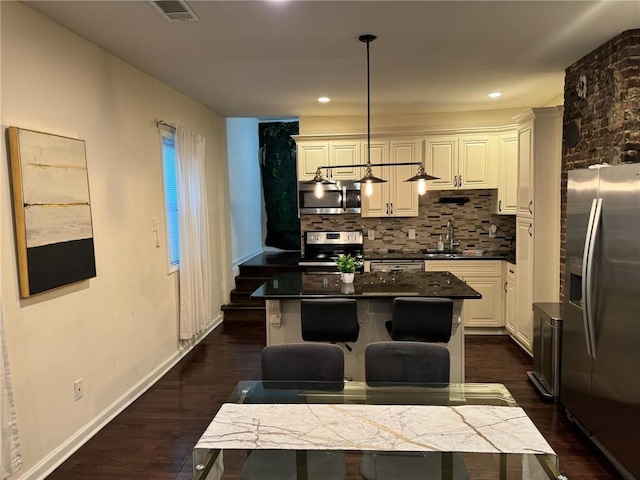 kitchen with pendant lighting, sink, backsplash, stainless steel appliances, and a kitchen island