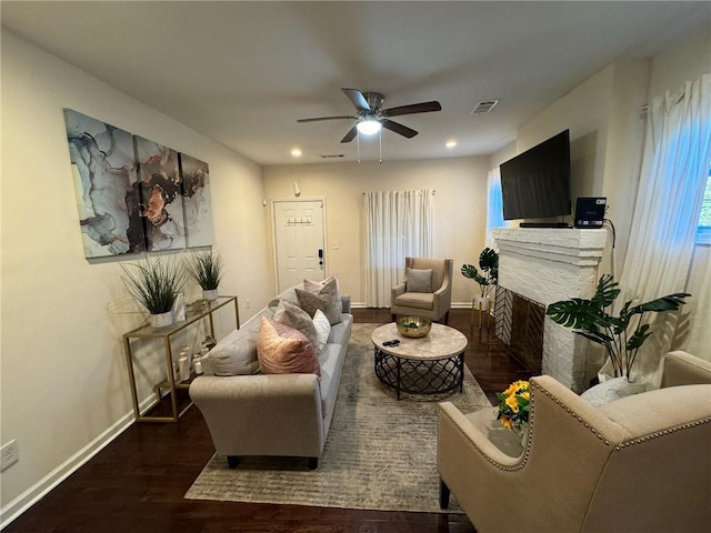 living room with ceiling fan, a stone fireplace, and dark hardwood / wood-style flooring