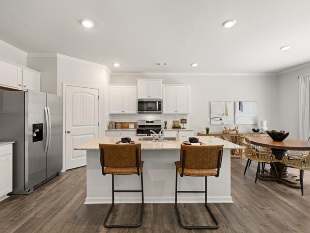 kitchen with white cabinets, crown molding, stainless steel appliances, and a kitchen island with sink