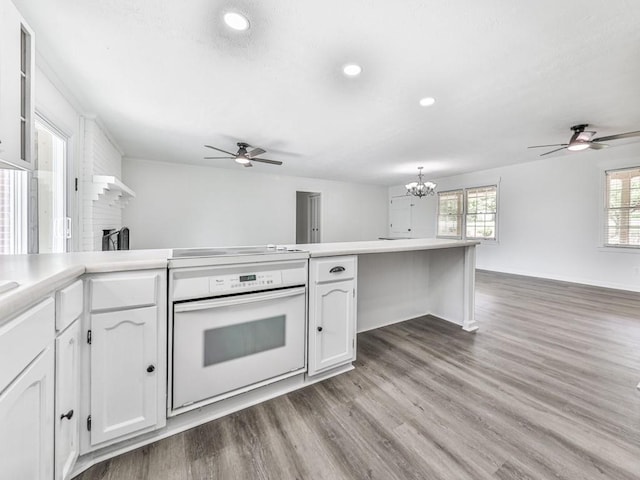 kitchen featuring oven, a ceiling fan, open floor plan, a chandelier, and white cabinetry