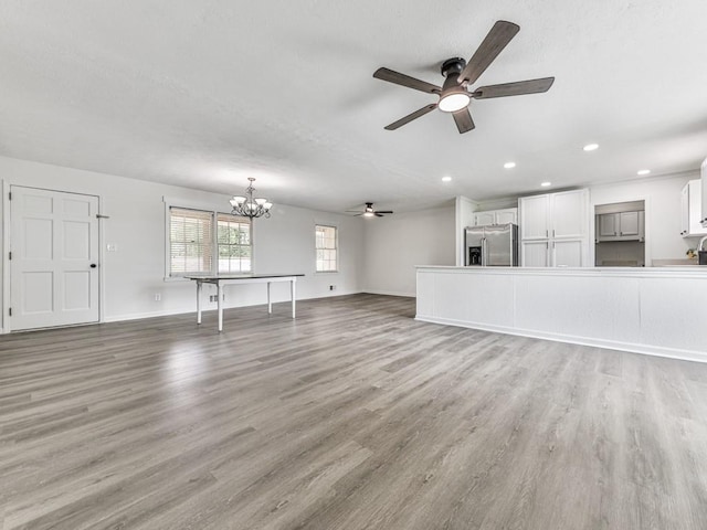 unfurnished living room with a ceiling fan, a chandelier, light wood-style floors, recessed lighting, and baseboards