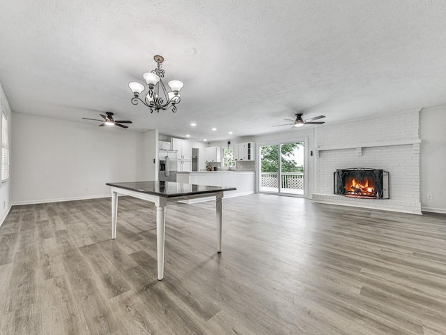 playroom featuring ceiling fan, a textured ceiling, a brick fireplace, a chandelier, and baseboards