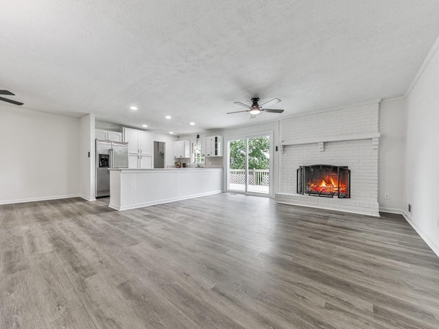 unfurnished living room with a ceiling fan, a textured ceiling, a brick fireplace, wood finished floors, and recessed lighting