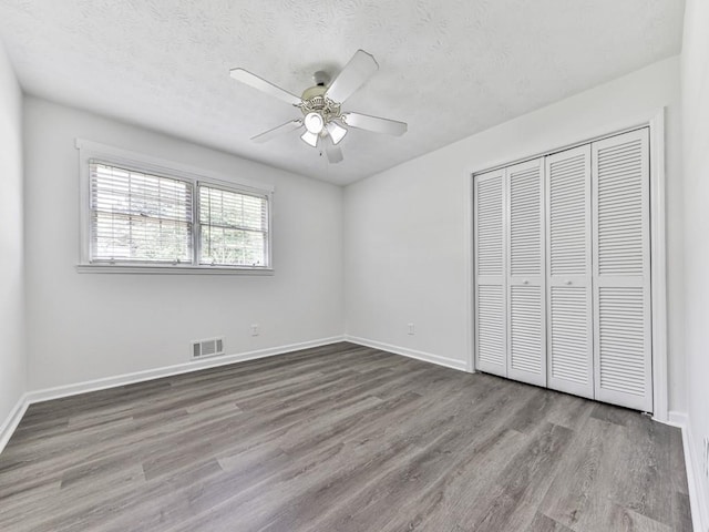 unfurnished bedroom featuring wood finished floors, a closet, baseboards, a textured ceiling, and ceiling fan