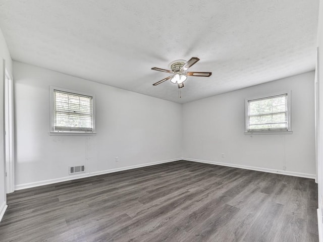 empty room featuring healthy amount of natural light, dark wood-style flooring, a ceiling fan, baseboards, and a textured ceiling
