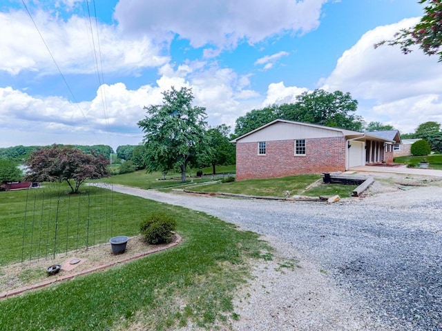 view of side of property with driveway, brick siding, an attached garage, and a yard