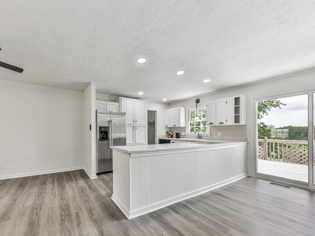 kitchen with stainless steel refrigerator with ice dispenser, a textured ceiling, a peninsula, a sink, and wood finished floors