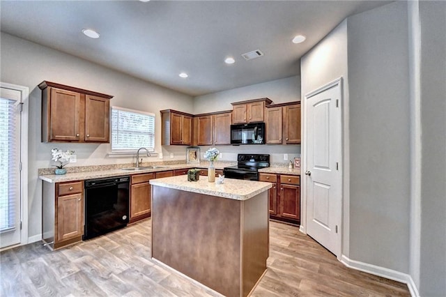 kitchen with black appliances, a kitchen island, sink, light stone counters, and light hardwood / wood-style flooring