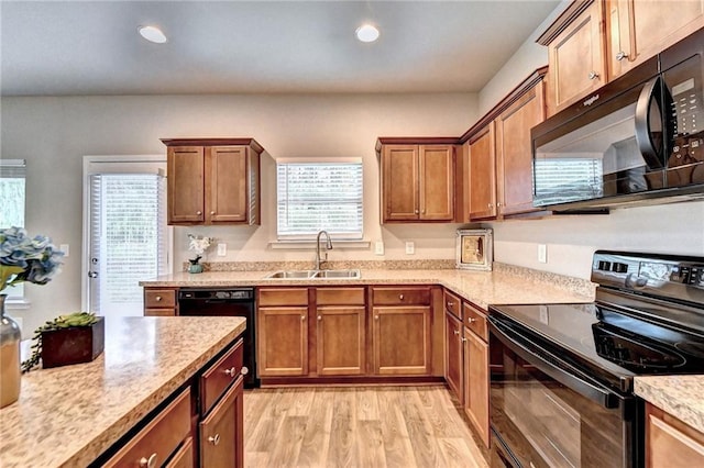 kitchen featuring sink, black appliances, light wood-type flooring, and a healthy amount of sunlight