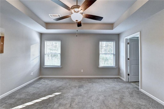 spare room featuring ceiling fan, light carpet, a raised ceiling, and a healthy amount of sunlight