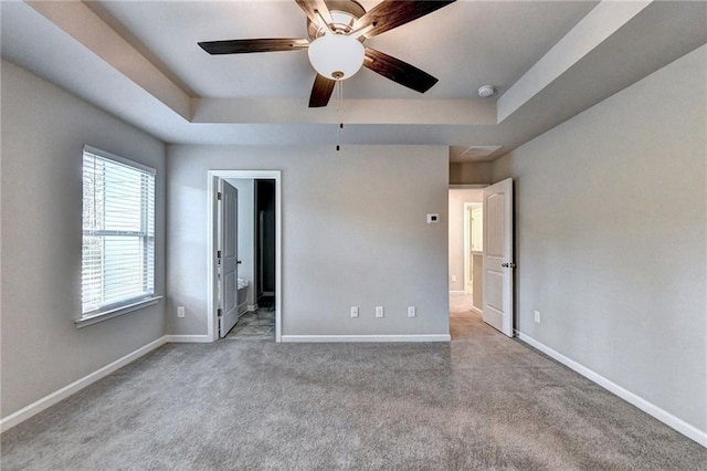 unfurnished bedroom with ceiling fan, a tray ceiling, ensuite bath, and light carpet