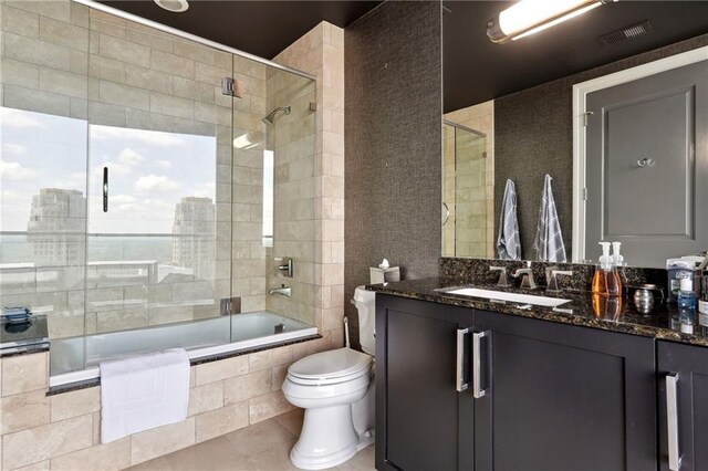 full bathroom with tile patterned flooring, vanity, bath / shower combo with glass door, and toilet