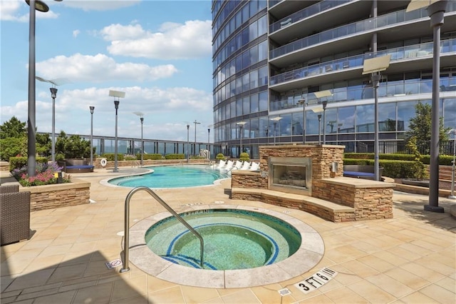 view of swimming pool featuring a patio area, a community hot tub, and an outdoor stone fireplace