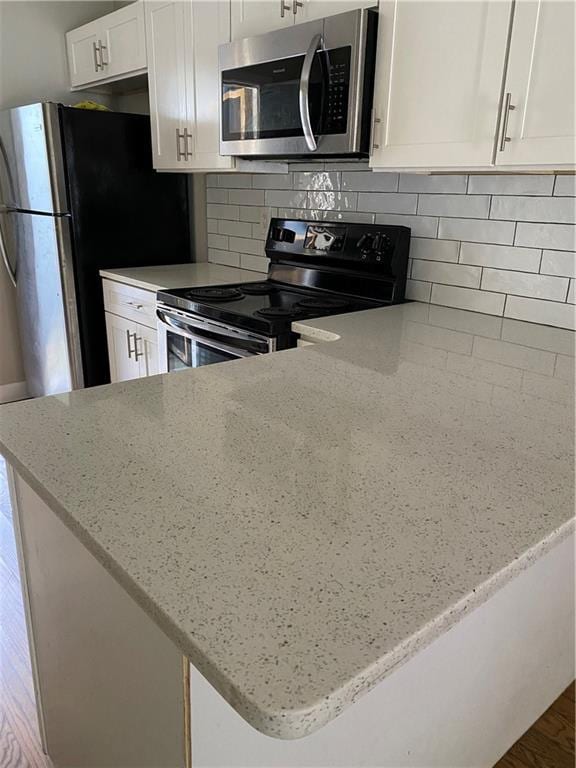 kitchen featuring white cabinetry, tasteful backsplash, wood-type flooring, light stone counters, and black electric range