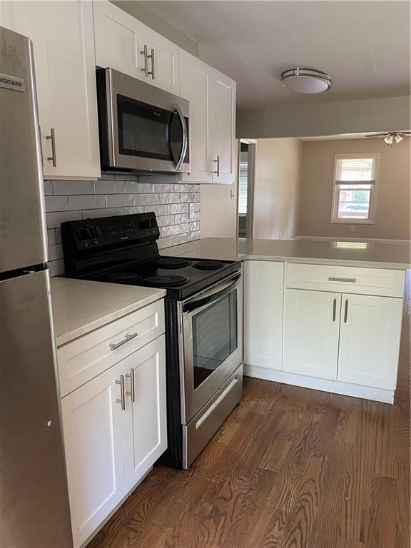 kitchen with white cabinets, decorative backsplash, kitchen peninsula, stainless steel appliances, and dark wood-type flooring