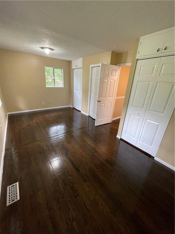 6399 Boca Grande Blvd, Forest Park, GA 30297 - unfurnished bedroom with two closets, baseboards, dark wood-style flooring, and a textured ceiling
