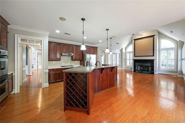 kitchen with a breakfast bar area, stainless steel appliances, decorative backsplash, a kitchen island with sink, and lofted ceiling