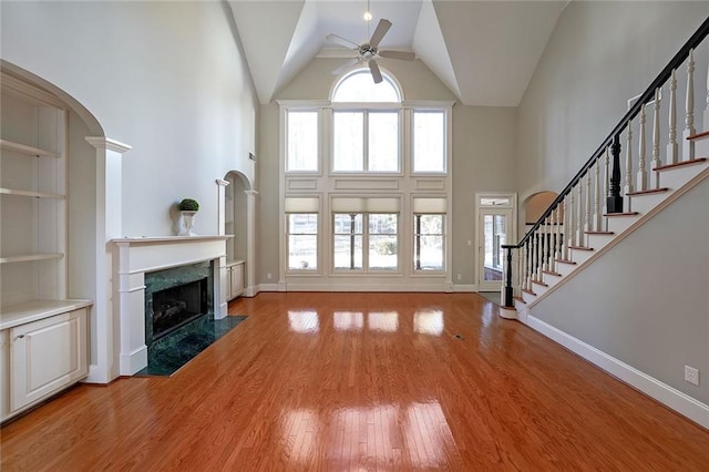 unfurnished living room with ceiling fan, light hardwood / wood-style flooring, a towering ceiling, and a fireplace