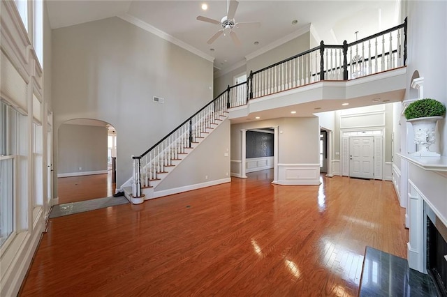 unfurnished living room with ceiling fan, crown molding, light hardwood / wood-style flooring, and a high ceiling