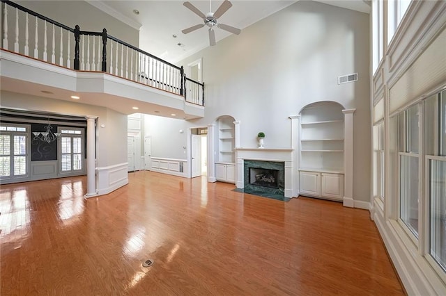 unfurnished living room featuring hardwood / wood-style floors, ceiling fan, a high ceiling, a fireplace, and built in shelves