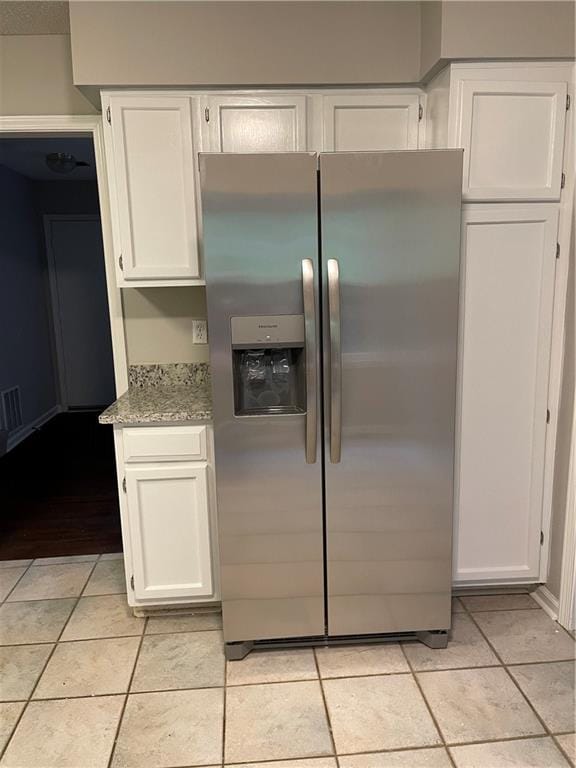 kitchen with white cabinets, light stone countertops, stainless steel fridge, and light tile patterned floors