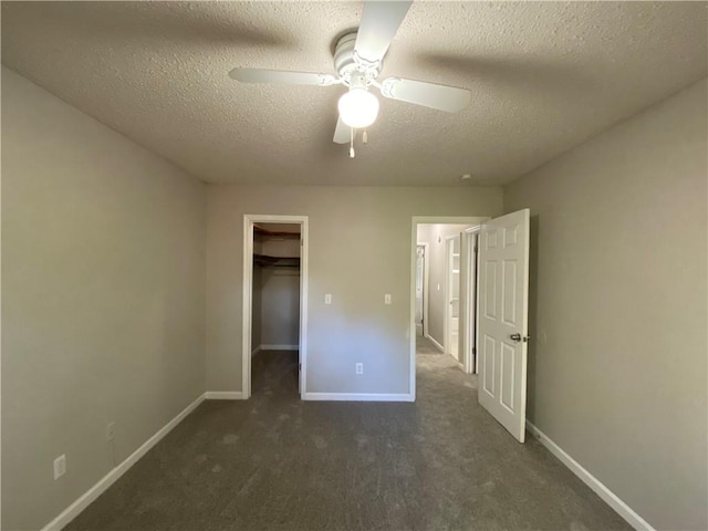 unfurnished bedroom with a walk in closet, a textured ceiling, dark carpet, and ceiling fan