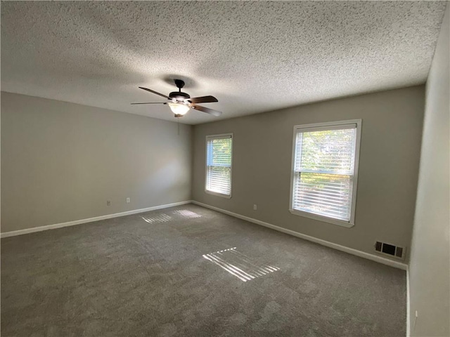 unfurnished room featuring a wealth of natural light, a textured ceiling, and dark carpet