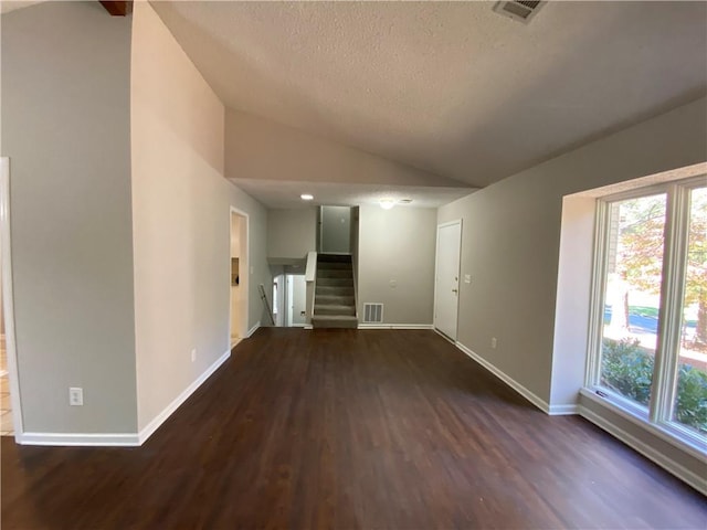 empty room featuring dark wood-type flooring, vaulted ceiling, and a textured ceiling