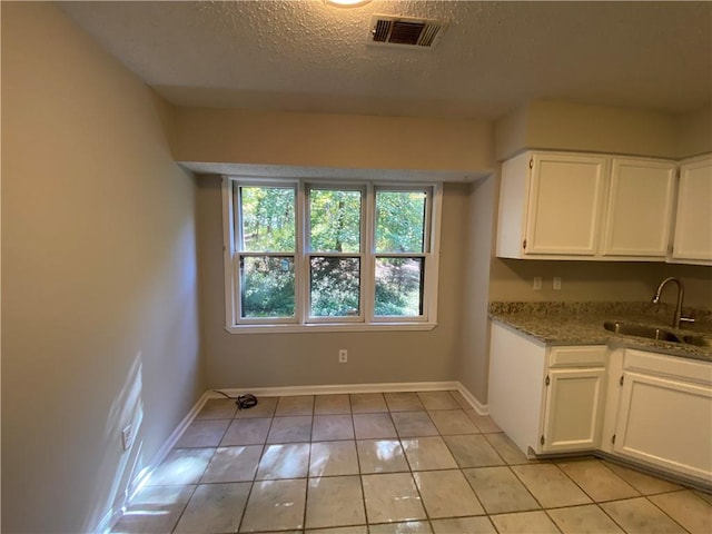 kitchen with stone countertops, sink, a textured ceiling, light tile patterned floors, and white cabinets