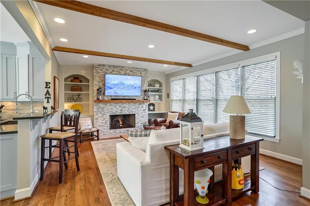 living room featuring light wood-style flooring, beam ceiling, ornamental molding, and a stone fireplace