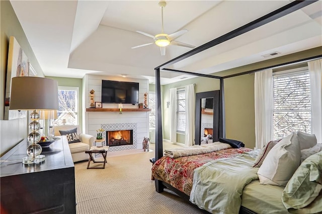 carpeted bedroom featuring a tray ceiling, a large fireplace, and visible vents