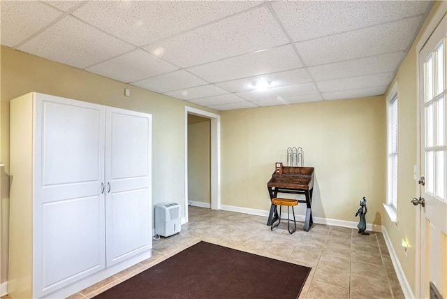 interior space featuring a paneled ceiling, light tile patterned floors, and baseboards