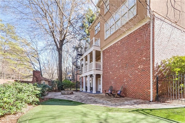 view of side of home featuring brick siding, an outdoor fire pit, a patio area, fence, and a balcony