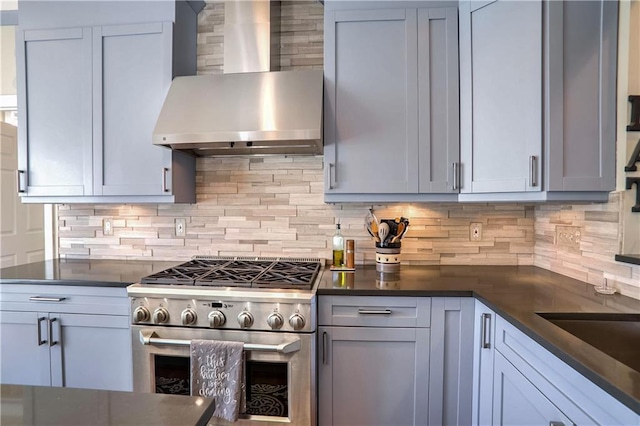 kitchen with wall chimney exhaust hood, high end stainless steel range, dark countertops, and decorative backsplash