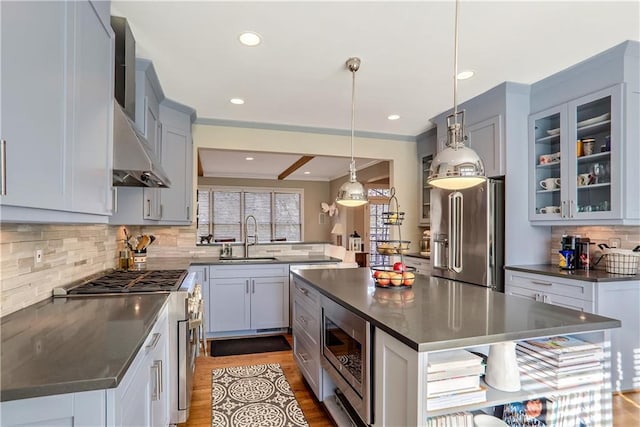 kitchen with pendant lighting, high end appliances, dark countertops, glass insert cabinets, and a sink