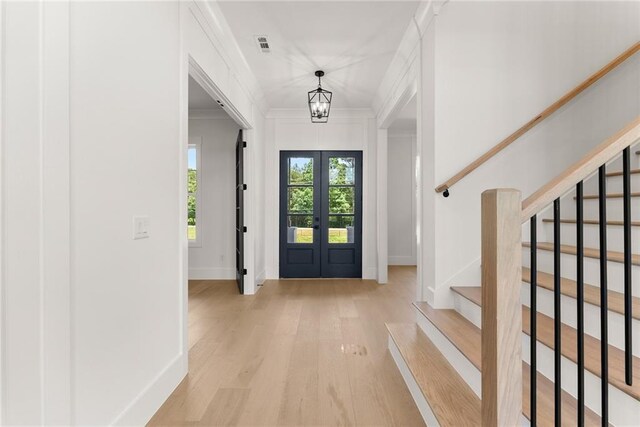 foyer entrance with a chandelier, french doors, light hardwood / wood-style flooring, and ornamental molding