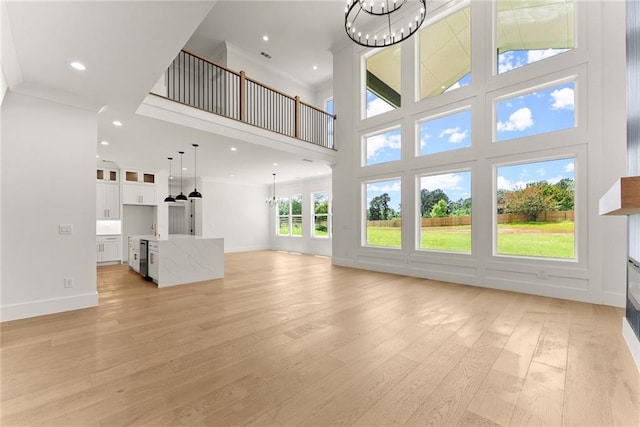 unfurnished living room featuring light wood-type flooring, a towering ceiling, and a chandelier