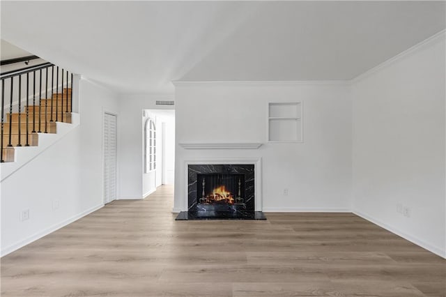 unfurnished living room featuring built in shelves, a fireplace, light hardwood / wood-style floors, and crown molding