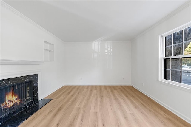 unfurnished living room featuring ornamental molding, built in shelves, a high end fireplace, and light hardwood / wood-style floors