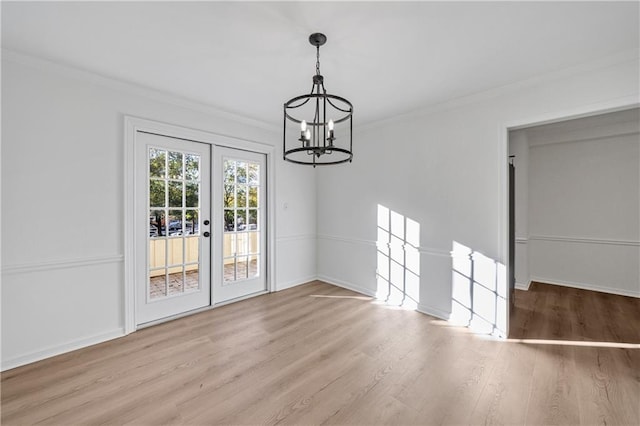 unfurnished dining area featuring an inviting chandelier, ornamental molding, french doors, and light wood-type flooring