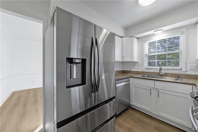 kitchen with sink, appliances with stainless steel finishes, white cabinetry, wood-type flooring, and decorative backsplash