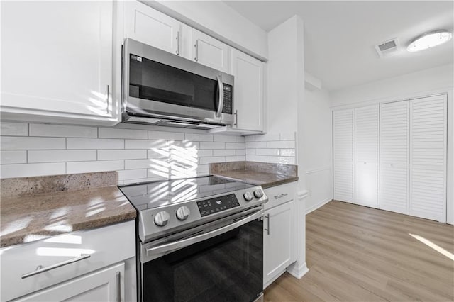 kitchen with white cabinetry, dark stone counters, light wood-type flooring, stainless steel appliances, and decorative backsplash