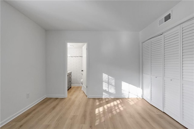 unfurnished bedroom with ensuite bathroom, light wood-type flooring, and a closet