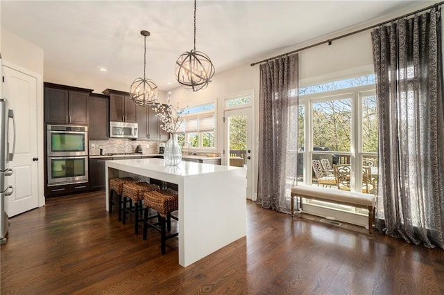 kitchen with pendant lighting, decorative backsplash, a center island, stainless steel appliances, and dark brown cabinets