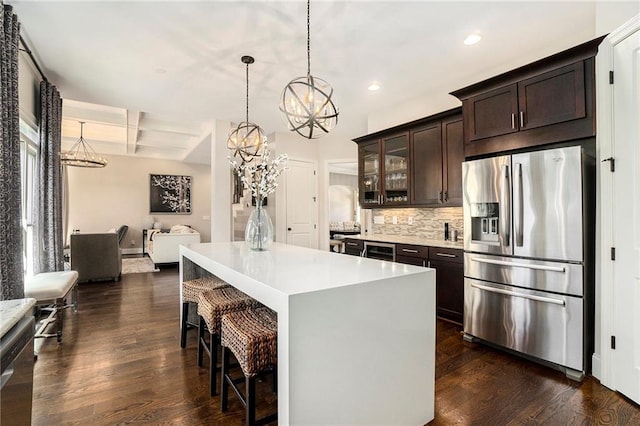 kitchen with dark brown cabinetry, decorative light fixtures, a kitchen island, stainless steel appliances, and backsplash