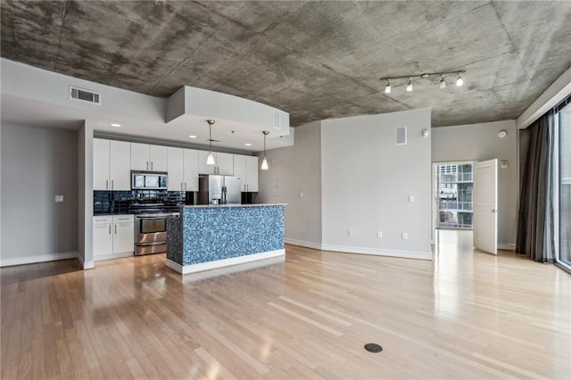 kitchen with decorative light fixtures, white cabinetry, decorative backsplash, a kitchen island with sink, and stainless steel appliances