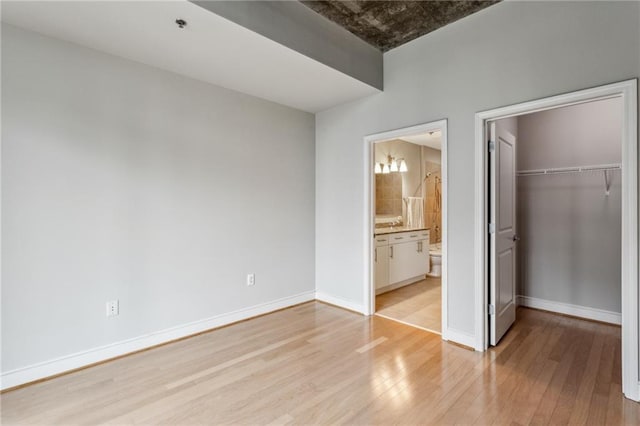 unfurnished bedroom featuring light wood-type flooring, a closet, and ensuite bathroom