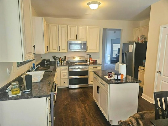 kitchen with appliances with stainless steel finishes, a sink, dark wood-style flooring, a center island, and dark stone countertops