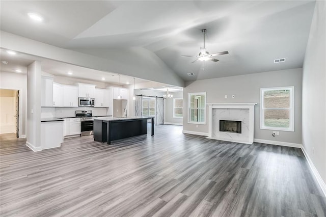 unfurnished living room with lofted ceiling, sink, ceiling fan, a premium fireplace, and wood-type flooring