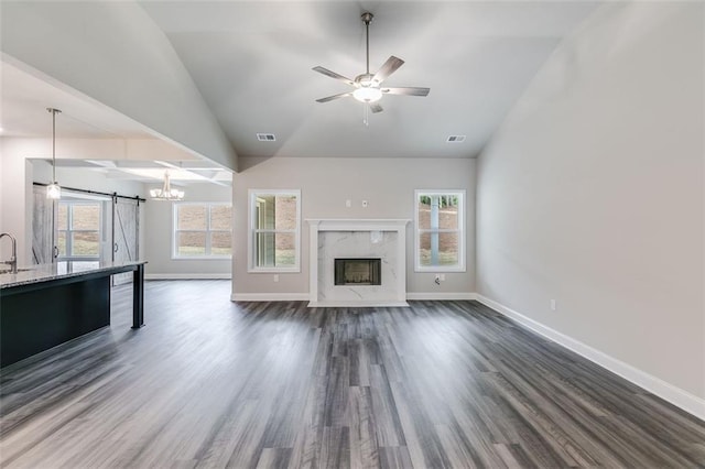 unfurnished living room with plenty of natural light, a barn door, dark hardwood / wood-style flooring, and lofted ceiling